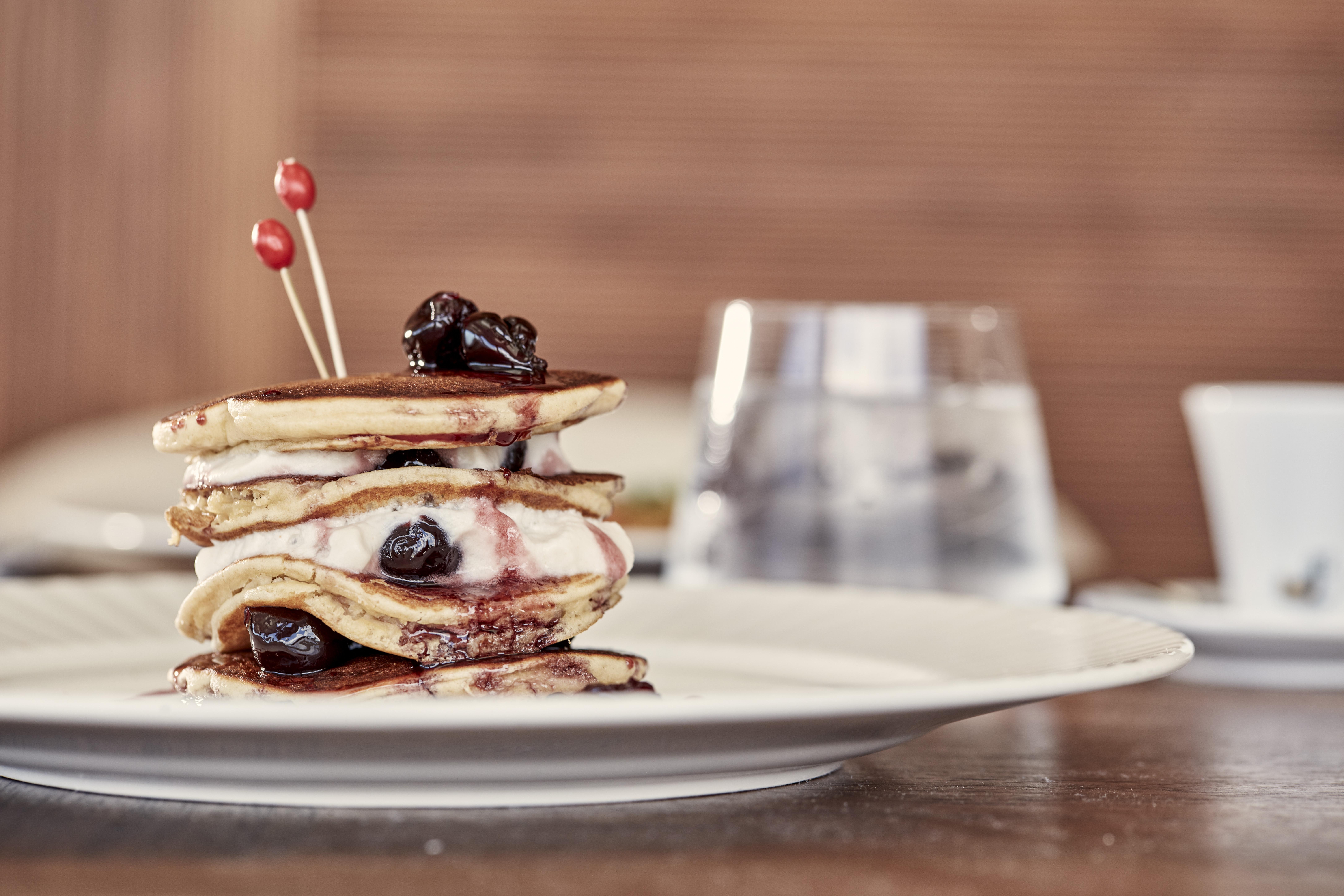Electra Metropolis Hotell Athen Eksteriør bilde The photo shows a stack of pancakes arranged on a plate. The pancakes are layered with a filling, possibly cream and fruit preserves or sauce, and topped with a few cherries or dark fruit. They are accented with two small red picks, giving it a decor
