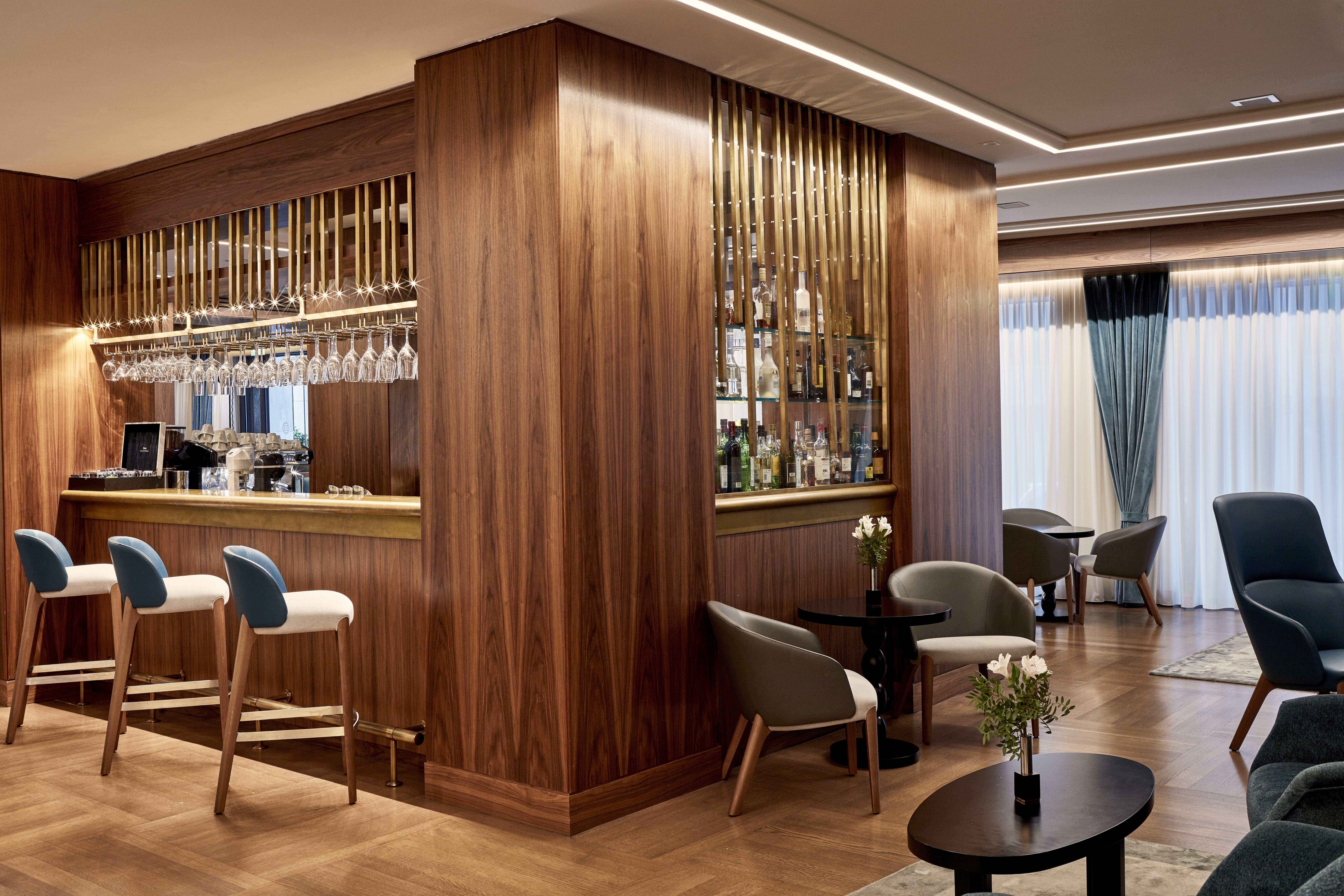 Electra Metropolis Hotell Athen Eksteriør bilde The photo depicts an elegantly designed bar area. The bar itself features a wooden structure with a display of various bottles and glassware, highlighted by warm lighting. In front of the bar, there are tall white and gray stools. The flooring is woo