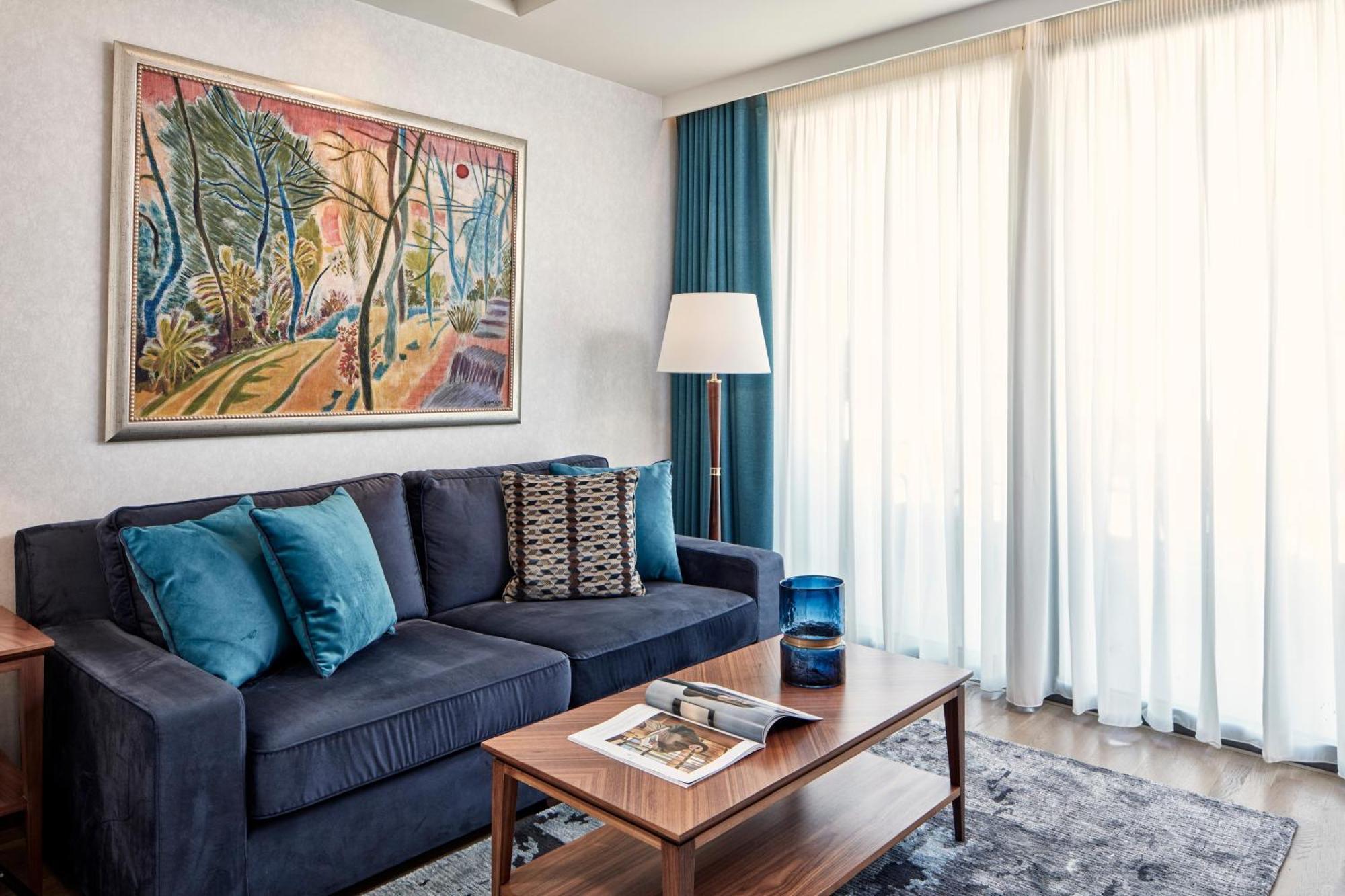Electra Metropolis Hotell Athen Eksteriør bilde The photo showcases a cozy living space. In the center, there is a dark blue sofa adorned with several teal and patterned throw pillows. A wooden coffee table is placed in front of the sofa, featuring a magazine on it. To the side, there is a modern 
